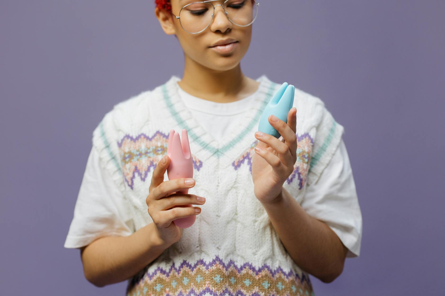 Woman holding blue and pink vibrators, considering how to introduce pleasure toys to a new partner