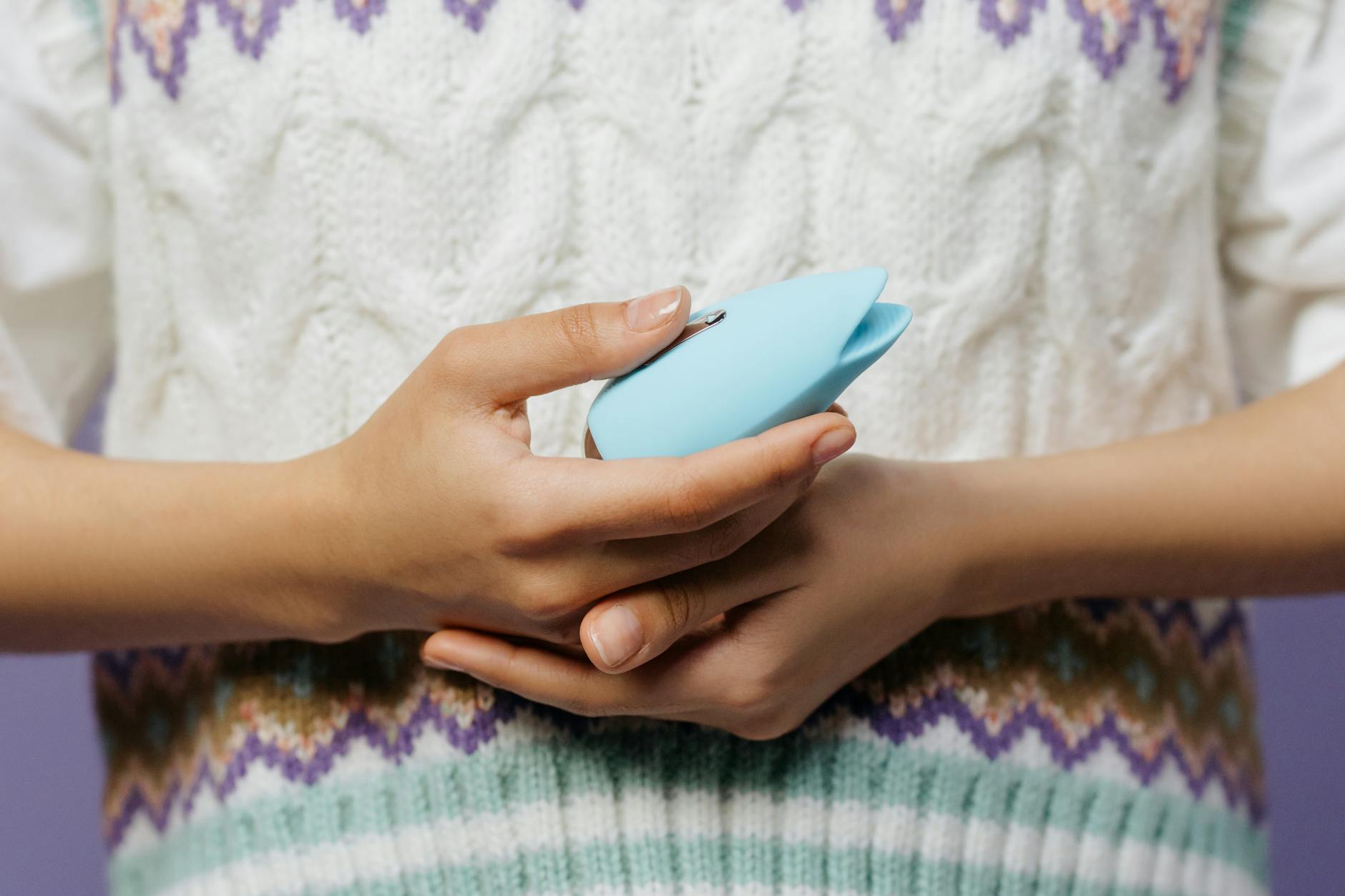 Hands holding a blue personal massager against a knitted sweater